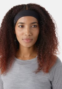 Diadema de tela negra que lleva puesta una persona con cabello rizado, con un detalle de botón. Se puede ver una camiseta gris jaspeada debajo.