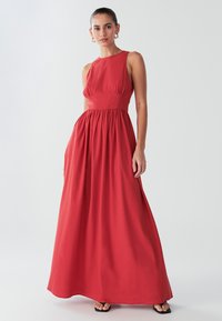 Vestito lungo rosso in tessuto leggero, con corpetto aderente a vita plissettata, scollo rotondo e gonna fluente.