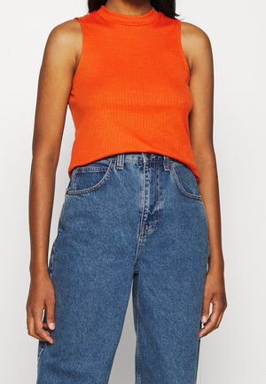 Femme portant un haut sans manches côtelé orange vif, rentré dans un jean en denim bleu taille haute avec poches avant.
