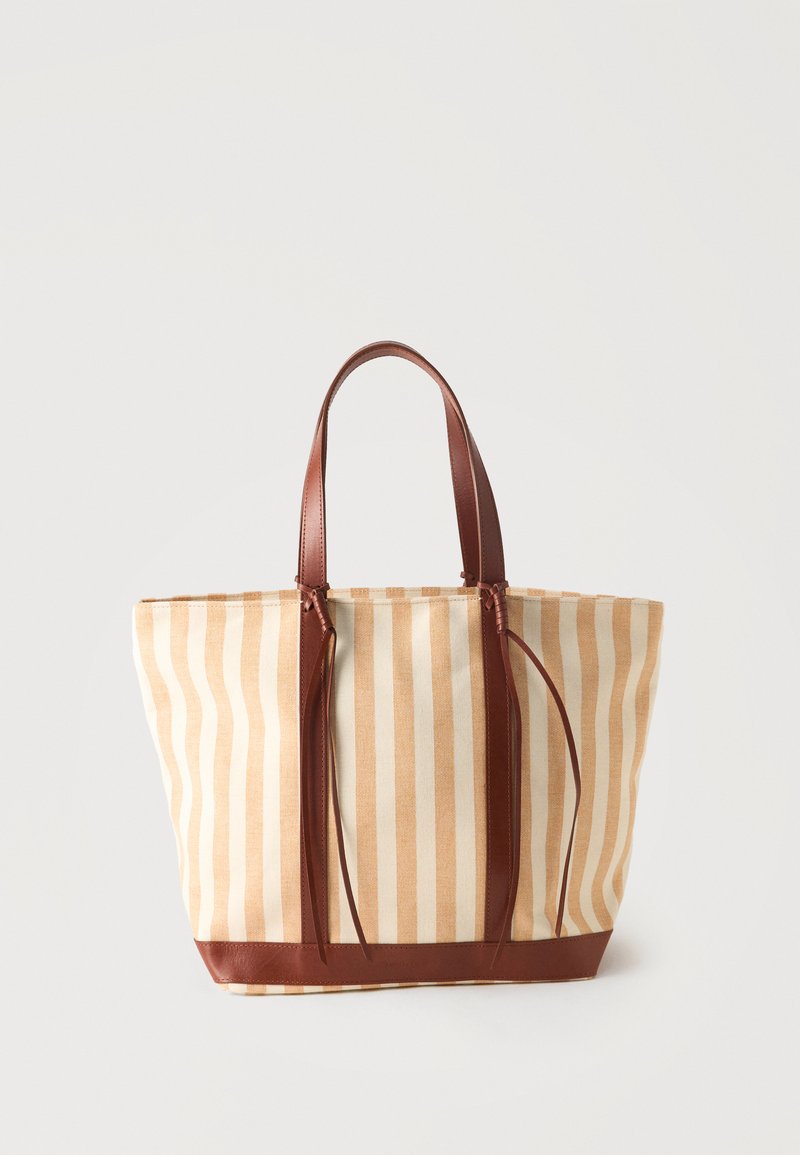 Sac cabas beige et blanc à rayures verticales avec anses et finitions en cuir marron, sur un fond clair uni.