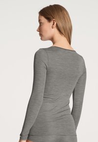 Maglia a maniche lunghe grigia in un morbido tessuto testurizzato con scollatura rotonda e design aderente, che mostra la vista dal retro.
