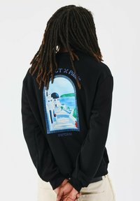 Sudadera negra con un gráfico de una escena de Santorini, con escalones que llevan a edificios blancos y una cúpula azul, y acentos florales rojos.