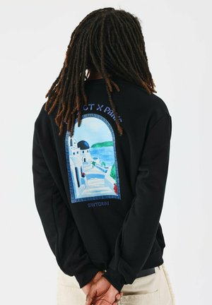 Sudadera negra con un gráfico de una escena de Santorini, con escalones que llevan a edificios blancos y una cúpula azul, y acentos florales rojos.