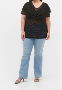 Svart spetsöverdel med lager på lager, skaldad halsringning, som kombineras med ljusblå raka jeans och sandaler med klack och remmar.