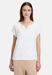 Top bianco a maniche corte con scollo a V, motivo floreale testurizzato e vestibilità comoda. Rifinito con un orlo leggermente curvo.