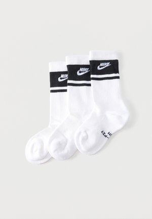 Tres pares de calcetines blancos hasta la pantorrilla con bandas negras y logotipos de Nike en los puños, dispuestos superpuestos sobre un fondo claro.