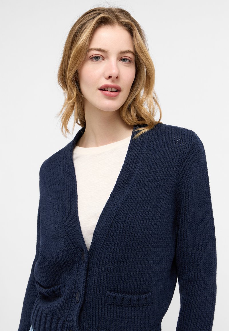 Marineblauer gestrickter Cardigan mit tiefem V-Ausschnitt, zwei vorderen Taschen und Knopfverschluss. Er hat einen strukturierten Stoff und eine lockere Passform.