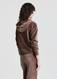 Felpa con cappuccio in velluto a coste marrone, con maniche lunghe e trama a coste. Caratterizzata da una vestibilità comoda, indossata con pantaloni abbinati.