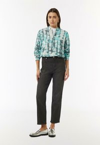 Hellblauer Batik-Zipper mit langen Ärmeln, schwarze gerade geschnittene Jeans und silberne Loafer. Die Jeans sind hoch geschnitten.
