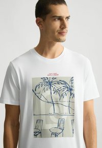 Tricou alb din bumbac cu un grafism reprezentând o palmier și un scaun albastre pe un fundal gri deschis; design clasic cu guler rotund.