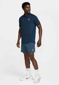 Navy polo shirt with a logo, paired with teal shorts. The outfit features a sleek, moisture-wicking fabric and a fitted silhouette.