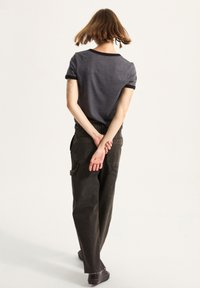 Mørkeblåt t-shirt med korte ærmer og sort kant, parret med løstsiddende sorte cargo-bukser med sidelommer og flossede kanter.
