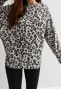 Sweter w nadruk w panterę z miękkiego materiału, o luźnym kroju, z długimi rękawami, okrągłym dekoltem i czarnymi akcentami na jasnym tle.