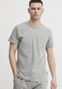 Graues T-Shirt mit kurzen Ärmeln aus strukturiertem Stoff, mit rundem Ausschnitt und einer Brusttasche auf der linken Seite. Leicht lockere Passform für komfortables Tragen.