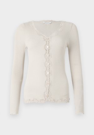 Cárdigan beige de canalé con mangas largas, escote en V, cierre de cinco botones y borde de encaje con volantes a lo largo de los bordes y la tapeta.