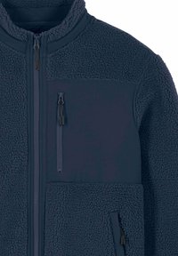 Veste polaire bleu marine avec col montant, fermeture éclair intégrale à l'avant, poche verticale sur la poitrine et poche latérale inférieure zippée.