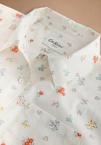 Biela košeľa na gombíky s farebnými malými kvetinovými a srdcovými vzormi, s predným vreckom a štítkom Cath Kidston London vo vnútri goliera.