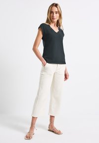 Svart texturerad V-ringad topp i kombination med krämfärgade vida byxor och beige strappy sandaler. Klara linjer och avslappnad passform genom hela outfiten.