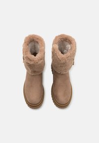 Brune semskede støvler med fluffy beige foring rundt kragen, gummisåle og lynlåsdetaile. Teksturen er blød med en glat overflade.