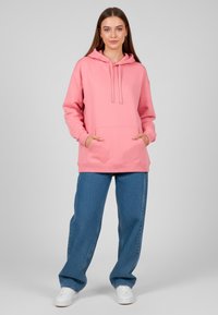 Felpa rosa con cappuccio e tasca a marsupio, abbinata a jeans blu larghi e sneaker bianche. Design casual e texture del tessuto morbida.
