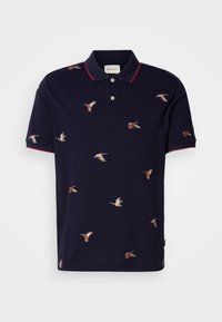 Marineblå polo med rød krave og mansjetter, prydet med broderte ender i forskjellige posisjoner over stoffet. Laget av bomull.
