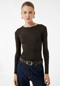 Bruine langemouwen fitted top gemaakt van gladde stof, gecombineerd met high-waisted donkerdenim jeans en een bruine riem met een gouden gesp.