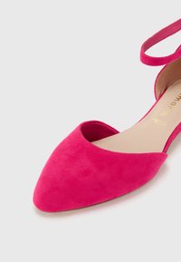 Fuksjowe zamszowe baleriny z ostrym noskiem, otwartymi bokami i paskiem na kostce. Wkładki wewnętrzne są beżowe z złotym tekstem.