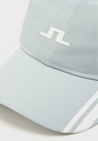 Lysegrå caps laget av ripstop-stoff, med en hvit logo, buet skygge og to hvite striper langs sidene som aksent.
