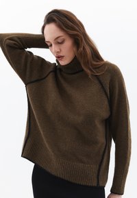 Bruine wollen turtleneck trui met geribbelde zoom en contrasterende donkere stiksels. Kenmerkt zich door een losse pasvorm en asymmetrisch design, met een soepel textuur.