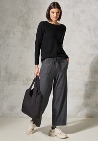 Schwarzes geripptes Langarmshirt, graue weite Sweatpants mit Taschen, schwarze Stofftragetasche und beige Sneakers mit dunklen Akzenten.