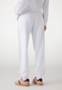Witte joggerbroeken met roze zijkanten, elastische manchetten en zakken, gemaakt van zachte stof. Draagt het met lichtroze sneakers.