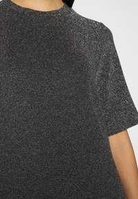 Top negro de manga corta con una tela texturizada y brillante. Presenta un cuello alto y un corte holgado, resaltando el brillo del material.