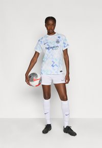 Balta futbola krekla ar gaiši zilu ģeometrisku rakstu, ar Nike logotipu un "betsson sport" zīmolu, apvienota ar baltām šortiem un melnbaltiem sporta apaviem.