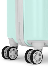 Licht turquoise harde koffer met een gestructureerd oppervlak, witte ritssluiting en vier dubbele spinnerwielen met zwarte rubberen banden.