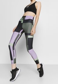Legginsy w geometryczny wzór w odcieniach czerni, zieleni i fioletu. Wykonane z elastycznego materiału, podkreślają wysoką talię i dopasowany krój.