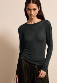 Schwarzes Langarmshirt mit rundem Halsausschnitt, aus weichem Stoff, kombiniert mit dunklen, glänzenden, elastischen Hosen mit elastischem Bund. Glatte Textur, taillierte Passform.