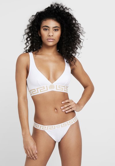 Ensemble de bikini blanc avec un décolleté plongeant, motif clé grec en or et détail de logo sur la bande. Texture lisse avec une couverture minimale.