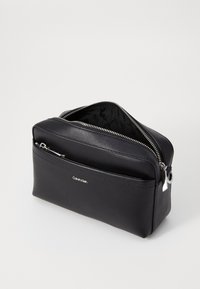 Borsa da toilette nera in pelle sintetica, forma rettangolare, con zip argentata e logo del marchio sul davanti. Superficie texturizzata, interni spaziosi.