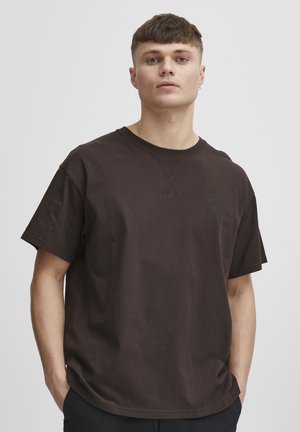 Camiseta de algodón marrón con un corte holgado, cuello redondo y mangas cortas. Presenta un logo impreso sutil y detalles de costura visibles.