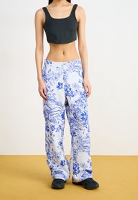 Svart avkortad tanktopp med tjocka axelband; blå och vita blommönstrade vida byxor med en texturerad tyg; svarta skor.