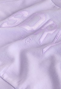 Svetlo fialová mikina s vyvýšeným vyšívaným textom "SORRY" v tučnom písmene, so soft, texturovanou tkaninou a rebrovaným výstrihom.