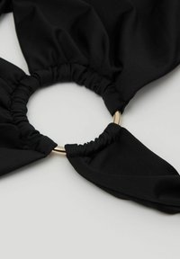 Black fabric scrunchie with elastic gathered around a gold metal ring on a white surface.