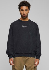 Zwarte crewneck sweatshirt met een vervaagde textuur, voorzien van een wit logo op de borst en geribbelde manchetten. Casual pasvorm met een rauwe zoom.
