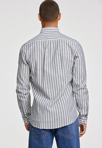 Camicia a maniche lunghe grigio e bianco a righe con colletto a punta, polsini con bottoni e orlo curvo, realizzata in tessuto leggero.