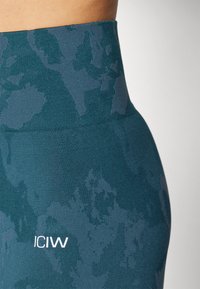 Hoog getailleerde teal leggings van textuurstof. Voorzien van een subtiel abstract patroon en een logo op de heup, wat het ontwerp versterkt.