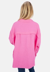 Übergroßes, pinkfarbenes Hemd aus strukturiertem Stoff, mit Kragen und herunterhängenden Schultern. Sichtbare Nahtdetails auf der Rückseite.