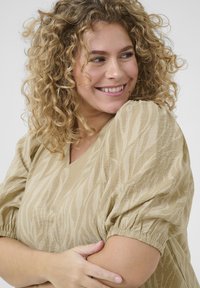 Blusa beige con escote en V y mangas cortas abullonadas. Presenta un patrón de textura en forma de ola. Tela suave con un corte holgado.