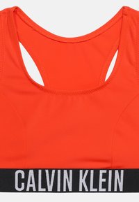 Φωτεινό πορτοκαλί αθλητικό σουτιέν με σχέδιο racerback και μαύρη ελαστική ταινία με λευκή επιγραφή λογότυπου Calvin Klein.