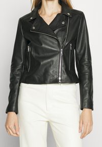 Svart läderkort jacka med dragkedjefickor, silverdetaljer och en något texturerad yta. Designad med en notch-krage och figursydda ärmar.