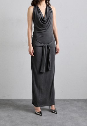 Grijze mouwloze maxi-jurk met een gedrapeerde halslijn en een ceintuureenheid in de taille, gemaakt van zachte, gestructureerde stof. Gecombineerd met puntige hakken.